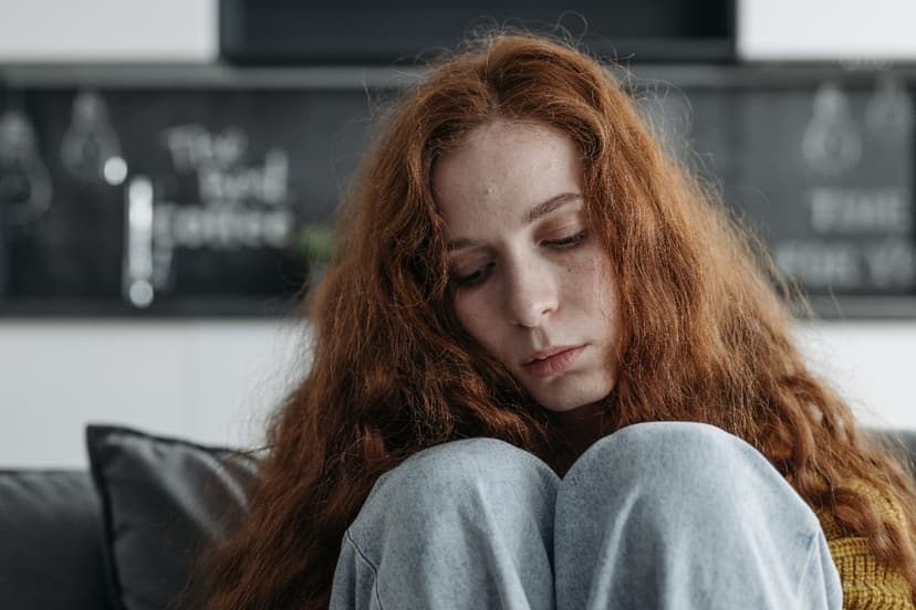 Withdrawn teenage girl with long red hair sitting on a couch hugging her knees and looking down, as a parent wonders whether it is teen depression or normal moodiness Withdrawn teenage girl with long red hair sitting on a couch hugging her knees and looking down, as a parent wonders whether it is teen depression or normal moodiness
