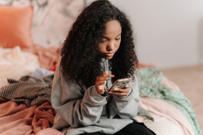 Teen girl sitting on her bed absorbed in her phone, illustrating everyday social media use and its effect on teen mental health Teen girl sitting on her bed absorbed in her phone, illustrating everyday social media use and its effect on teen mental health